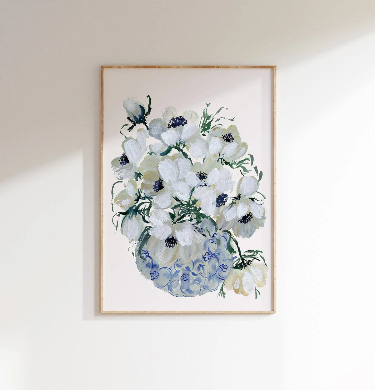 White anemone bouquet print in a light wood frame on a pale wall.