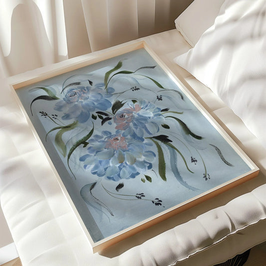 Blue ranunculus print in a light wood frame resting on a white chair in sunlight.