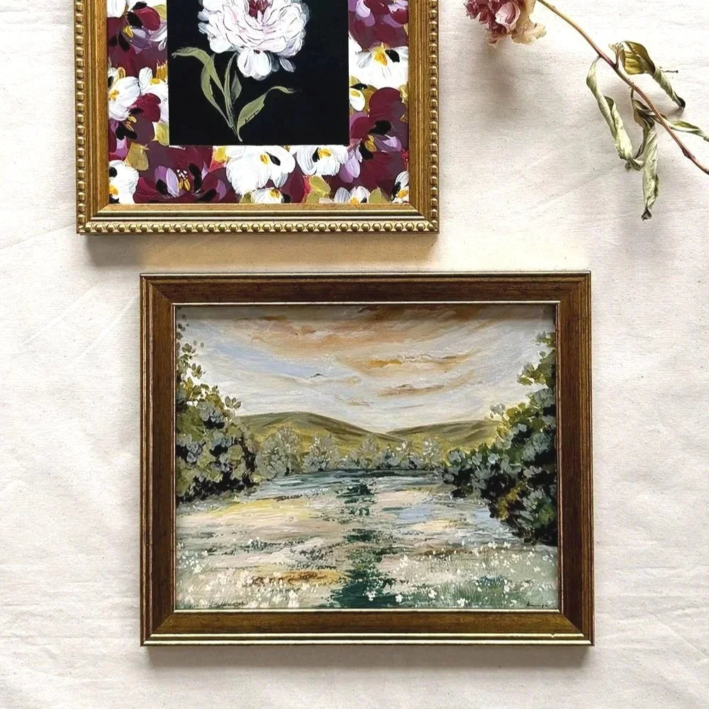 Two framed original art pieces The top frame features a floral painting with white flowers and burgundy leaves on a black background, bordered by a gold frame.
