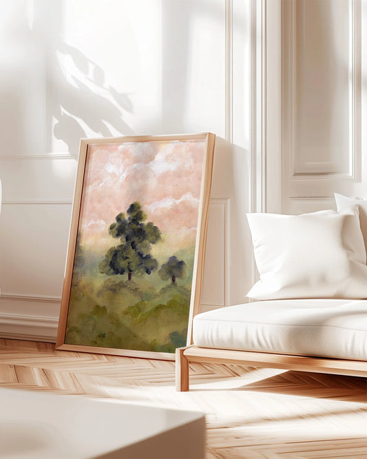 A framed landscape painting leaning against a white paneled wall in a bright, modern room with a white cushioned wooden chair and light wood herringbone flooring. Set in a modern interior, Art print by Ramya Rajiv