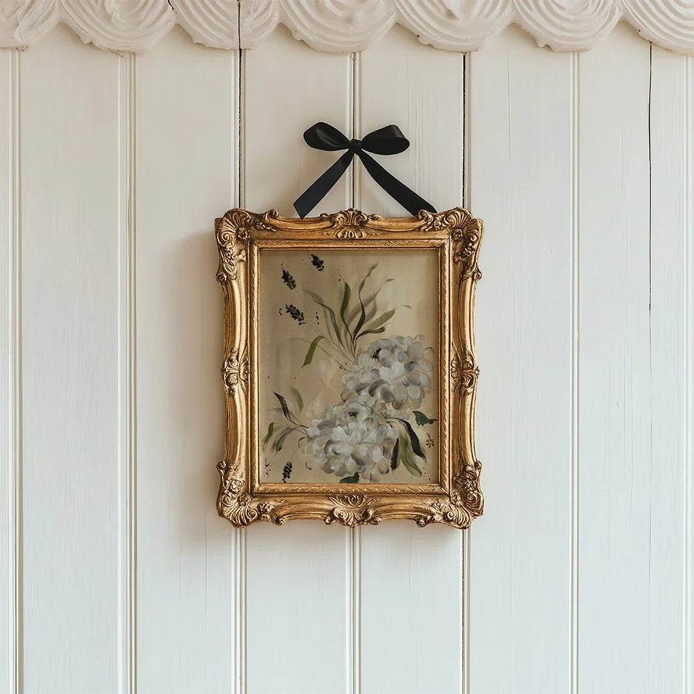 White dahlia print in an ornate gold frame suspended by a black bow on white panels.