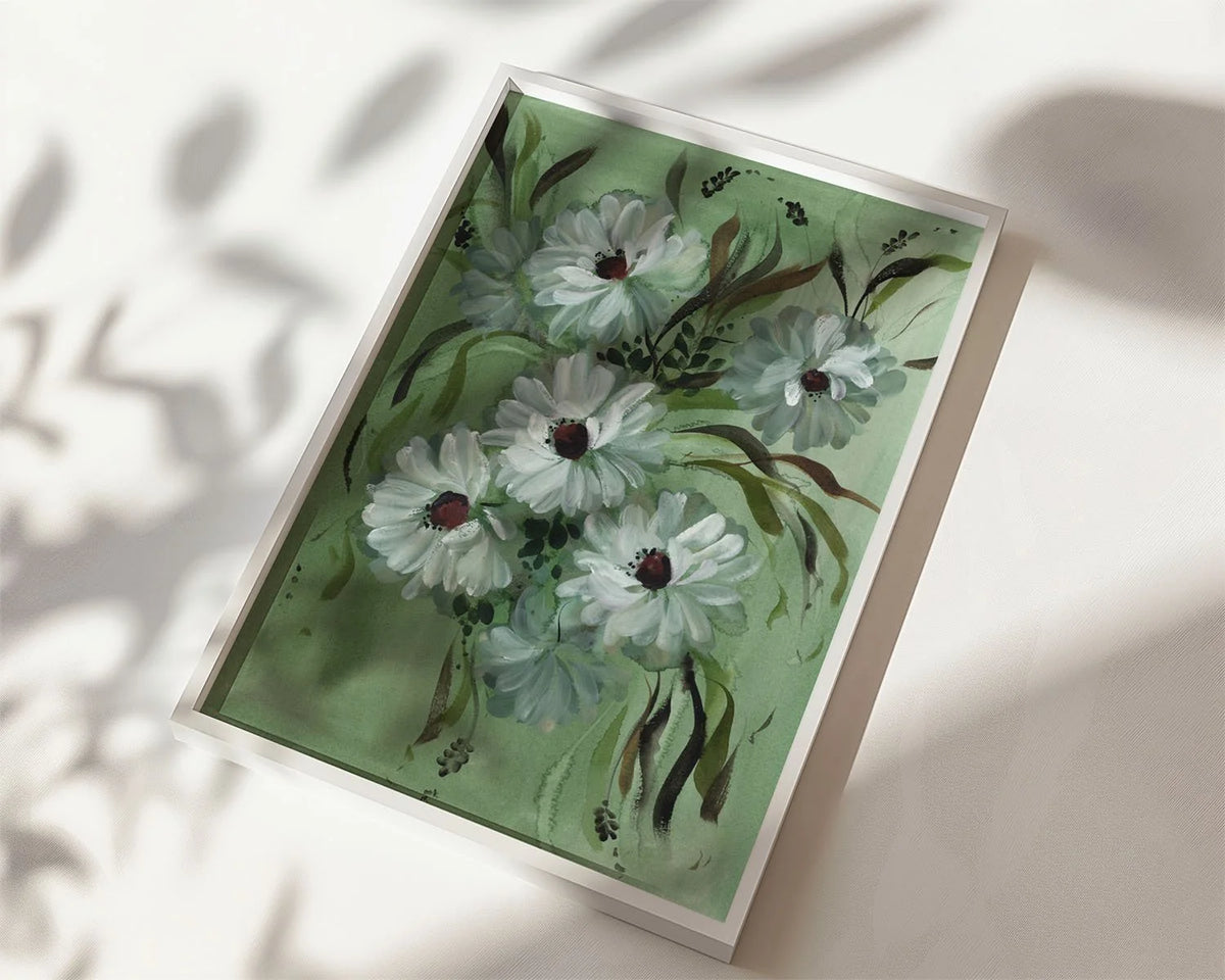 White daisy print on green in a white frame lying in sunlight with soft leaf shadows.