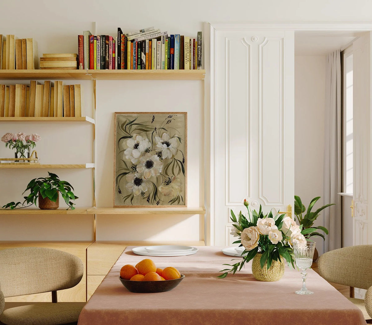 White anemone print displayed on a bookshelf behind a dining table with flowers and fruit.