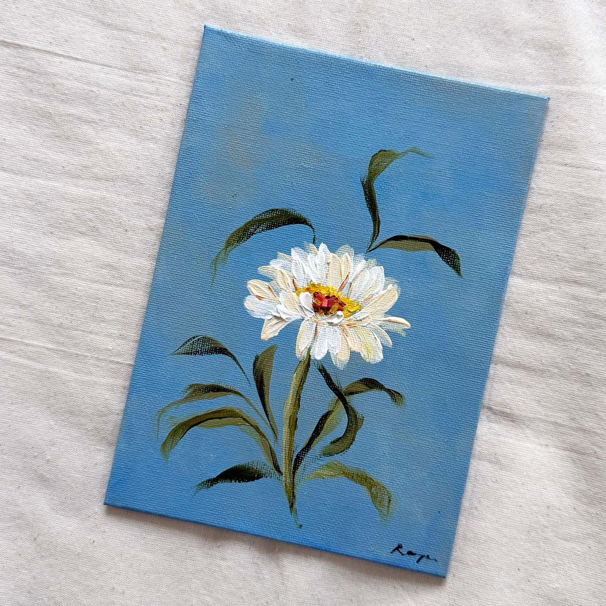 A small canvas original of a white daisy with green leaves on a blue background