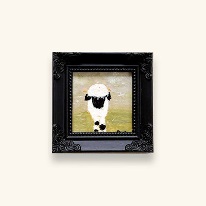 A small framed art original featuring a black and white sheep on a soft yellow-green background, enclosed in an ornate black frame 