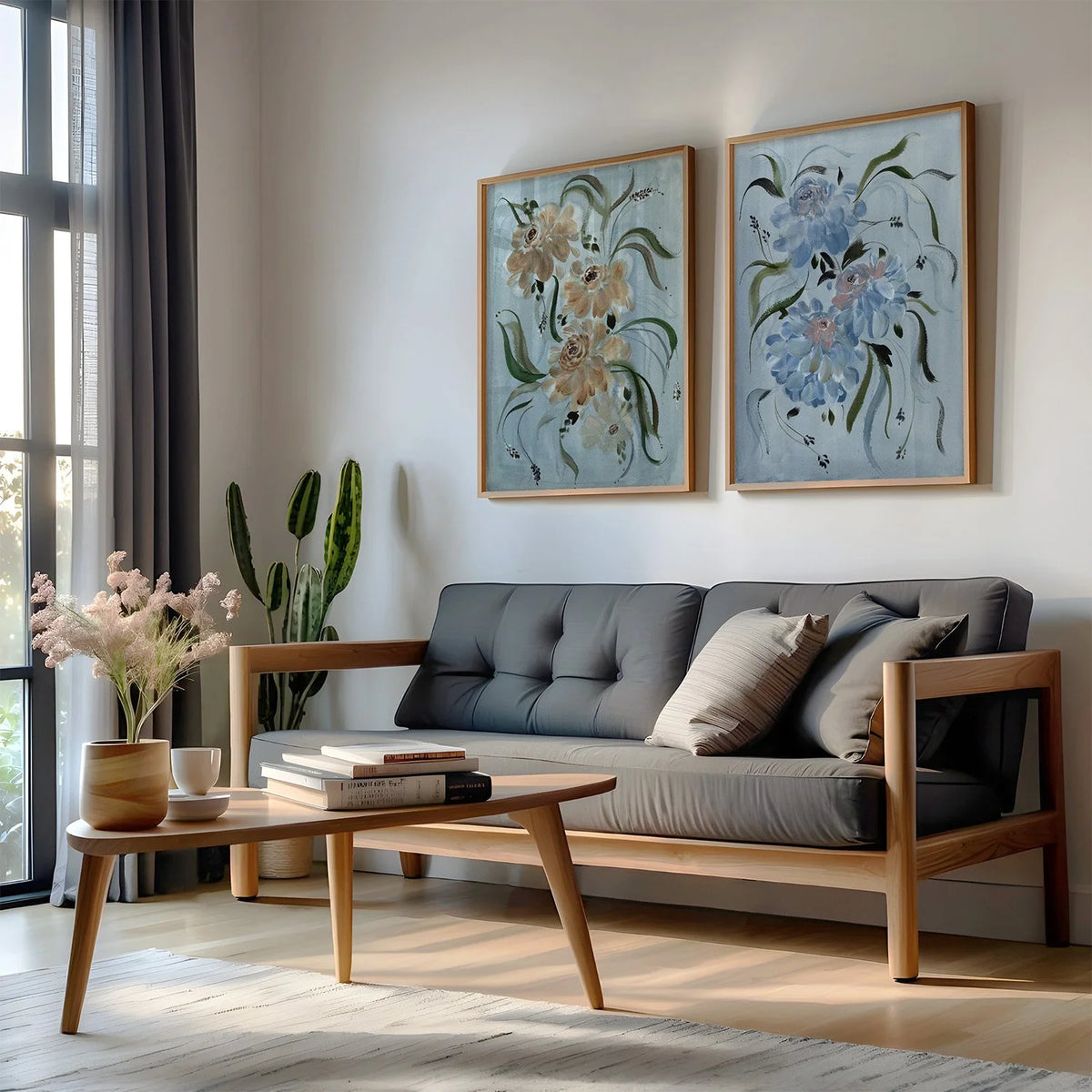 Brown and blue ranunculus prints in gold frames above a gray sofa beside a window.