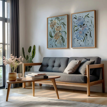 Brown and blue ranunculus prints in gold frames above a gray sofa beside a window.