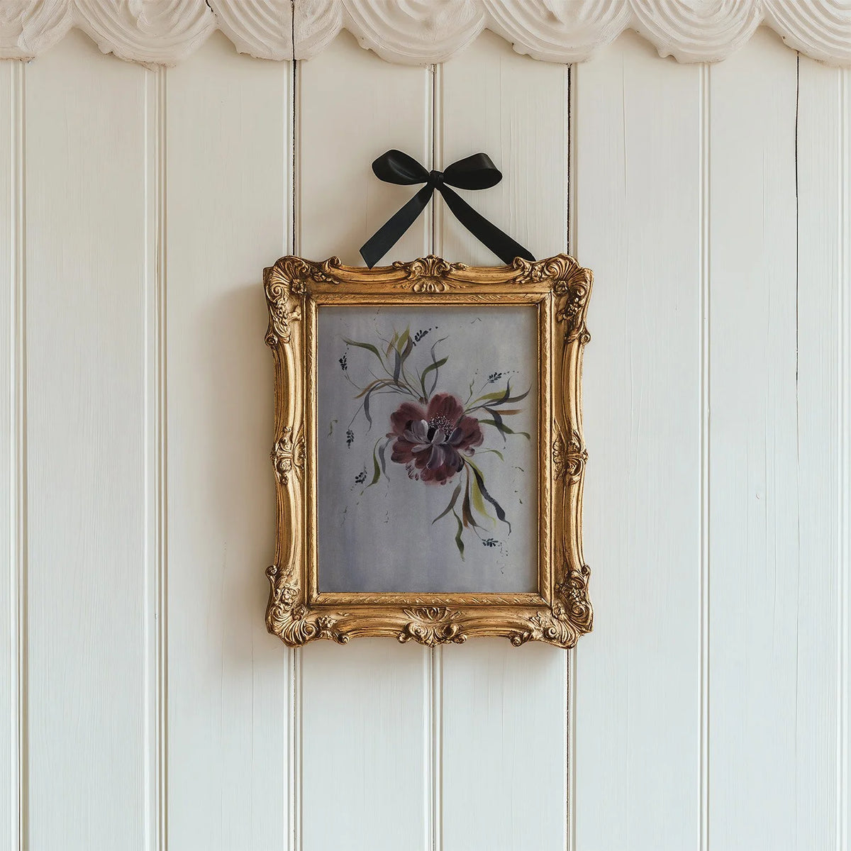 Burgundy anemone print in an ornate gold frame suspended by a black bow on white panels.