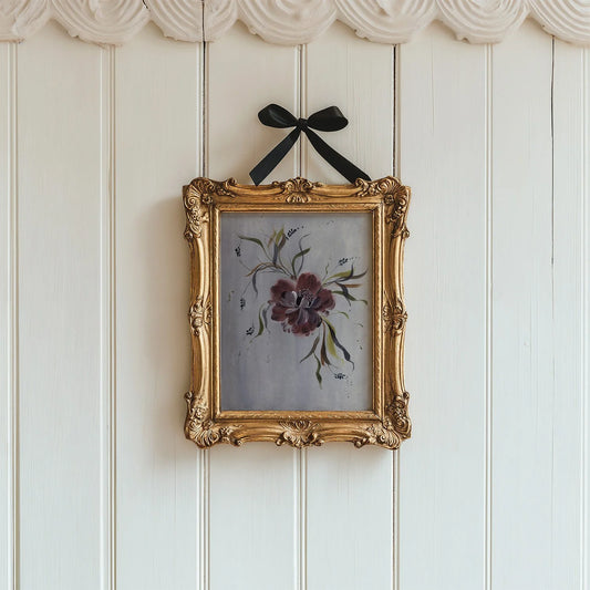 Burgundy anemone print in an ornate gold frame suspended by a black bow on white panels.