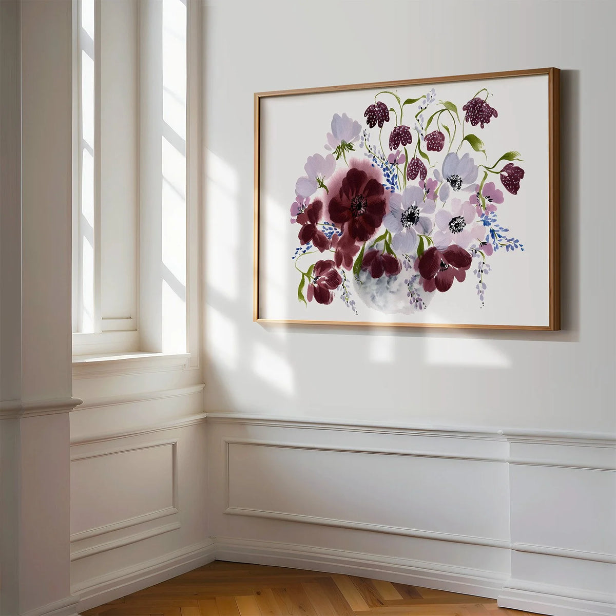 Horizontal burgundy floral vase print in a gold frame beside a sunlit window.