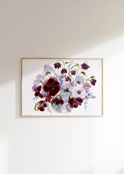 Horizontal burgundy and pale purple floral vase print in a light wood frame on a pale wall.