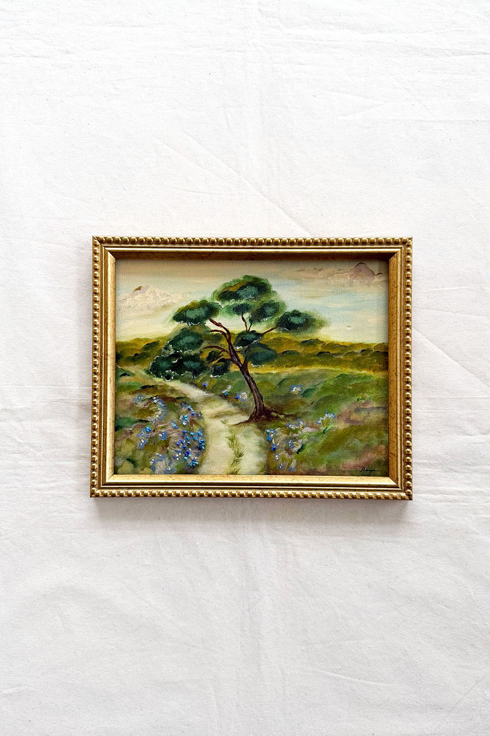 Original Landscape by ramya rajiv in a gold frame, the pastoral landscape shows a single tree along the path.
