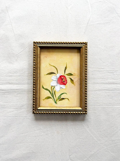 A small framed original floral painting featuring a Daffodil with white petals and green leaves on a yellow background, enclosed in an ornate gold frame 