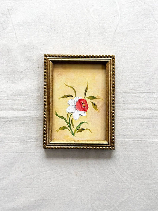 A small framed original floral painting featuring a Daffodil with white petals and green leaves on a yellow background, enclosed in an ornate gold frame 