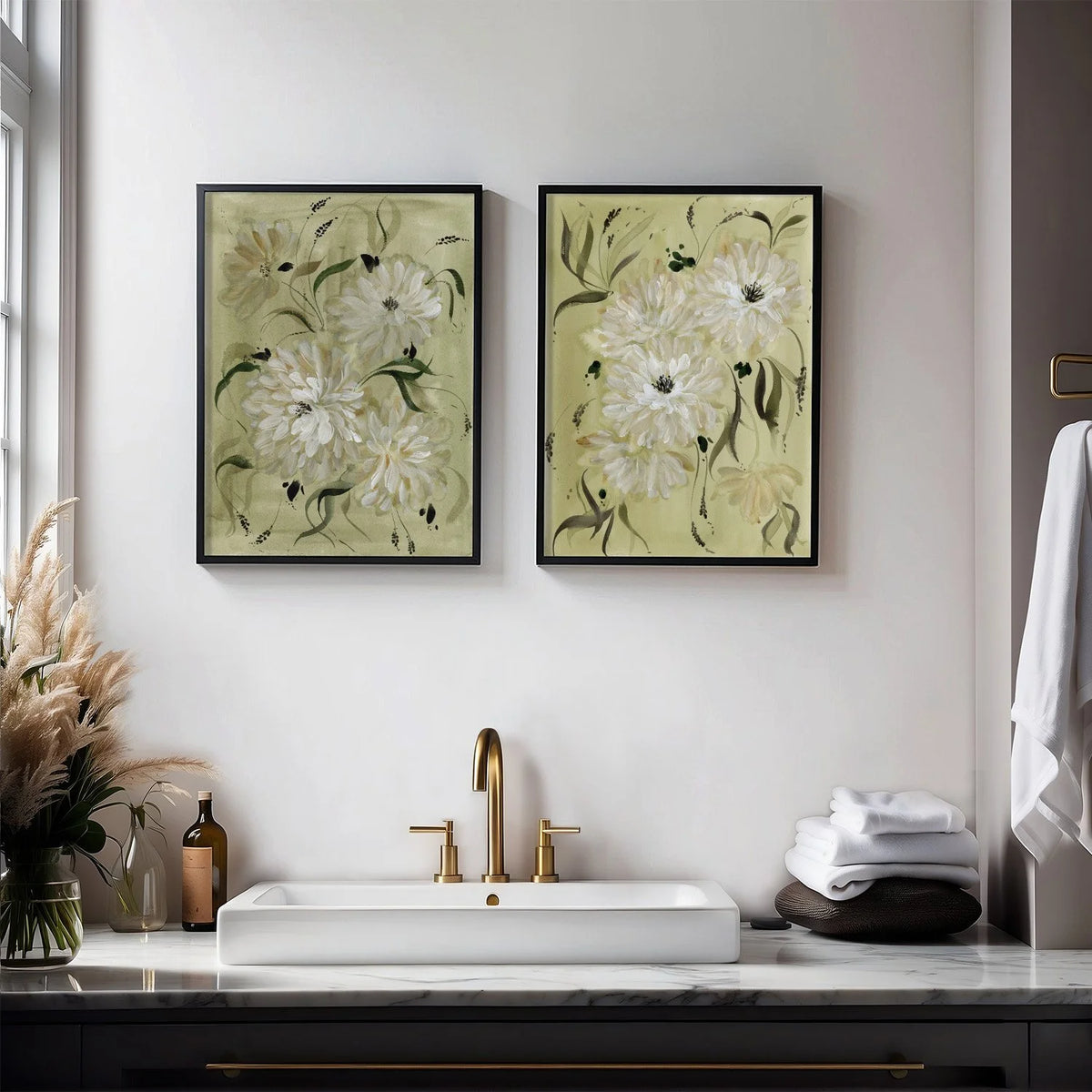 Pair of white dahlia prints in black frames above a bathroom sink with gold fixtures.