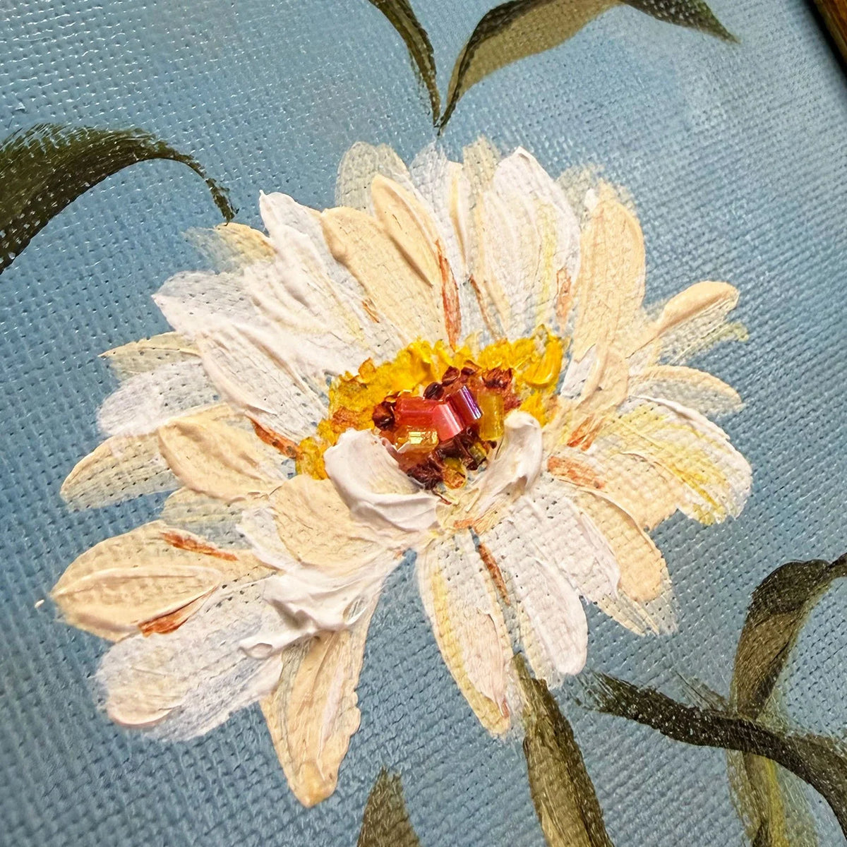 Close-up of a textured canvas original featuring a cream and white daisy with a yellow and orange center