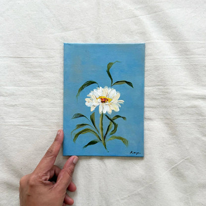 A original painting of a white daisy with green leaves on a blue background. April flower of the month