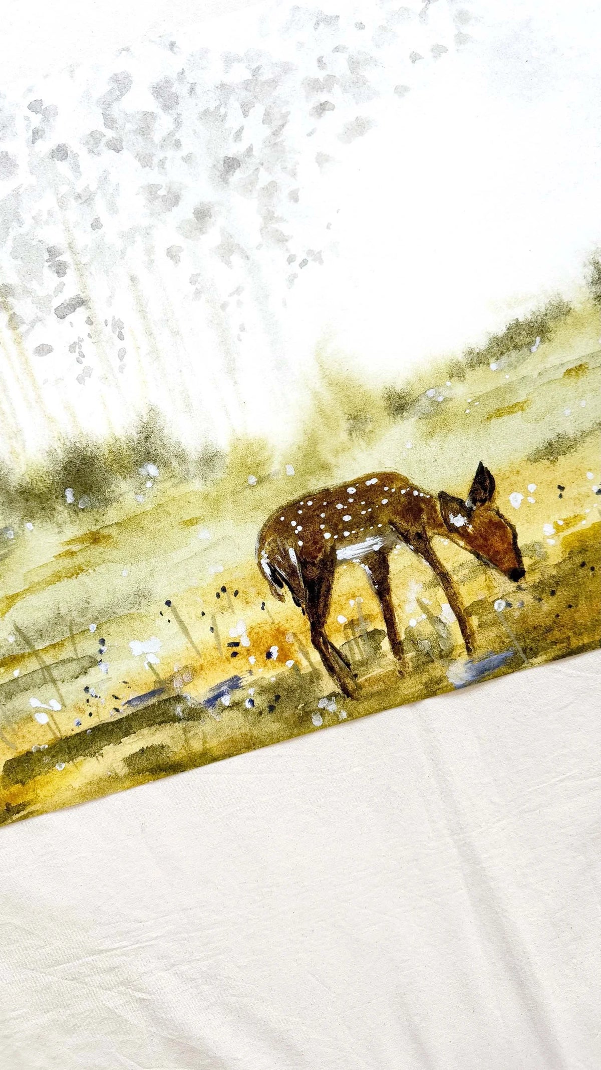 A watercolor-style art print or textile featuring a brown spotted deer standing in a golden field under a bright white sky with soft gray tree silhouettes.