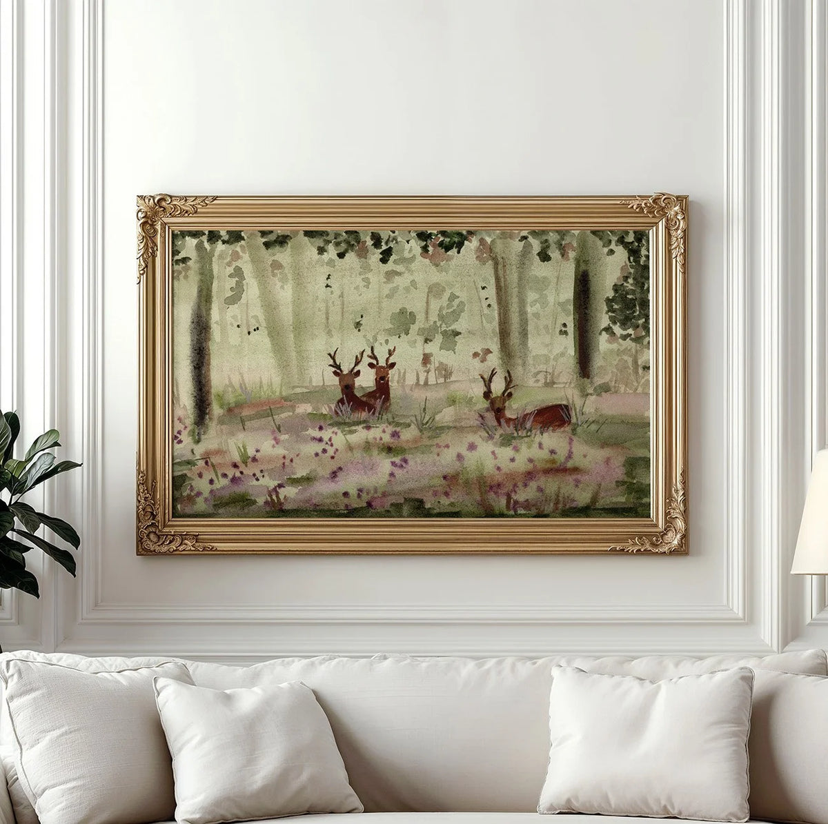 A framed watercolor painting of deer in a forest, displayed on a white wall above a white sofa with pillows.