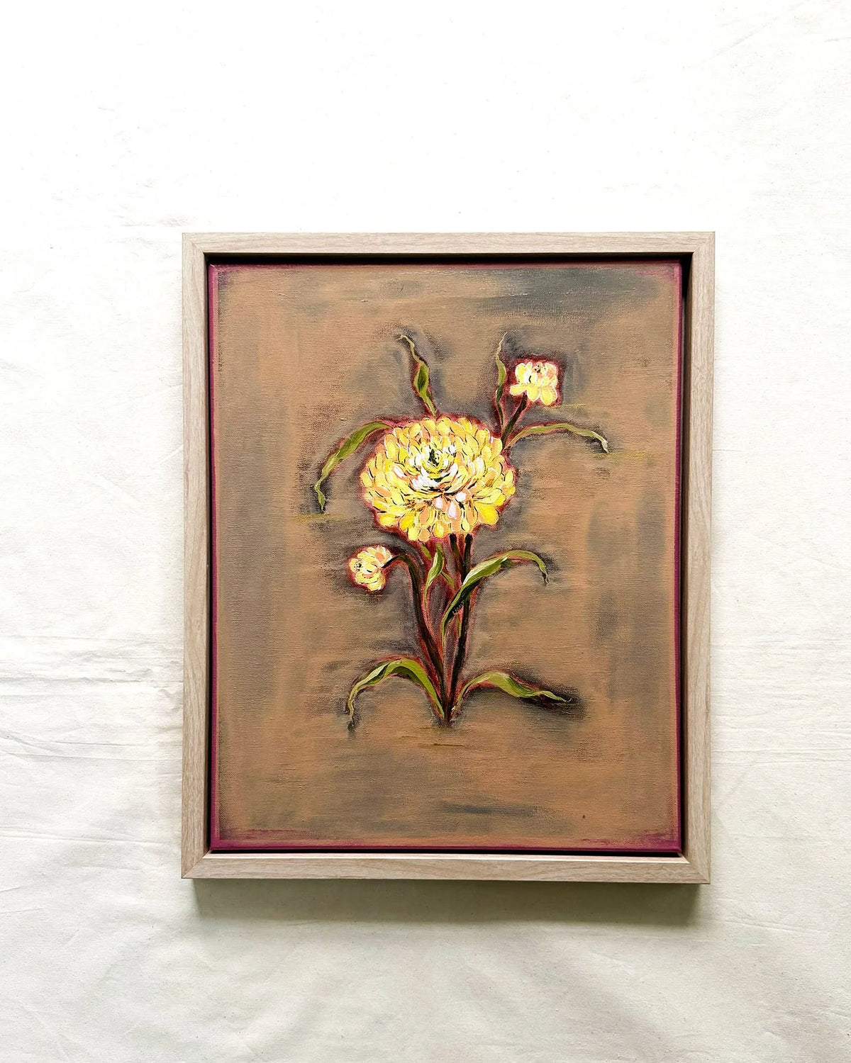 A framed painting of a yellow flower with green leaves on a textured brown background, housed in a light-colored wooden frame  Yellow Chrysanthemum on Earth Tones