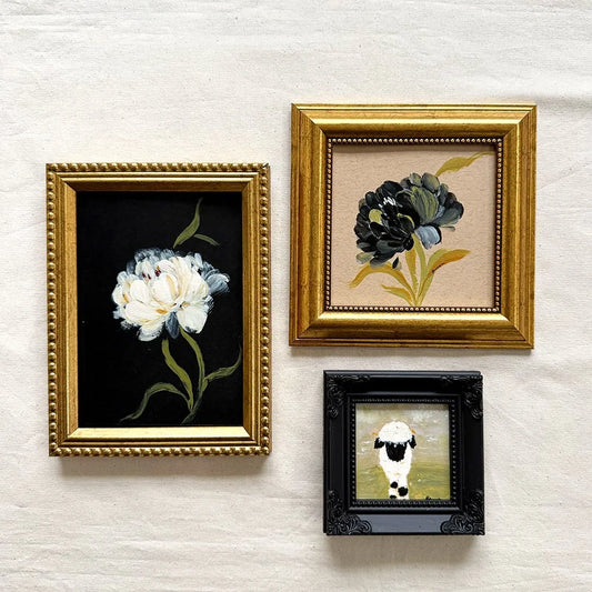 Three framed art originals of florals and farm animals. The top-left print features a white flower on a black background in a gold frame.