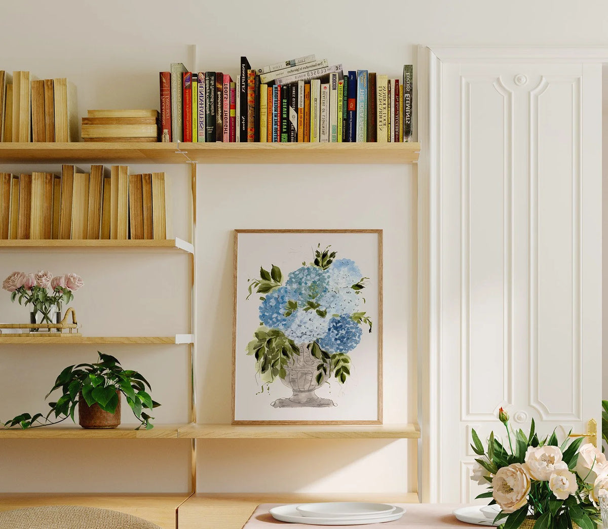 Blue hydrangea vase print displayed on a bookshelf beside books and plants.