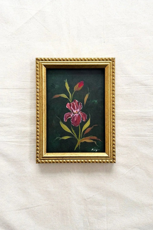 A small framed original of a pink iris flower with green and yellow leaves on a dark background, set in a decorative gold frame 