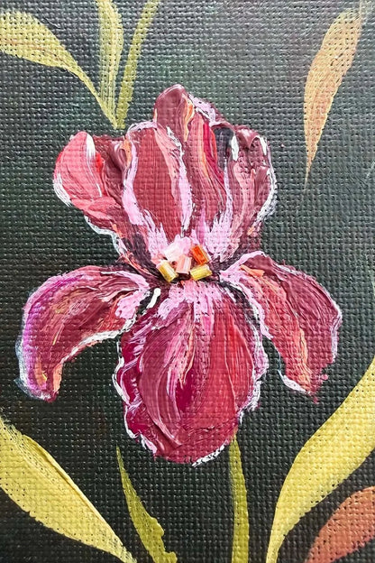 Close-up of a painted iris with layered pink and magenta petals, yellow-green leaves, and a dark textured background.
