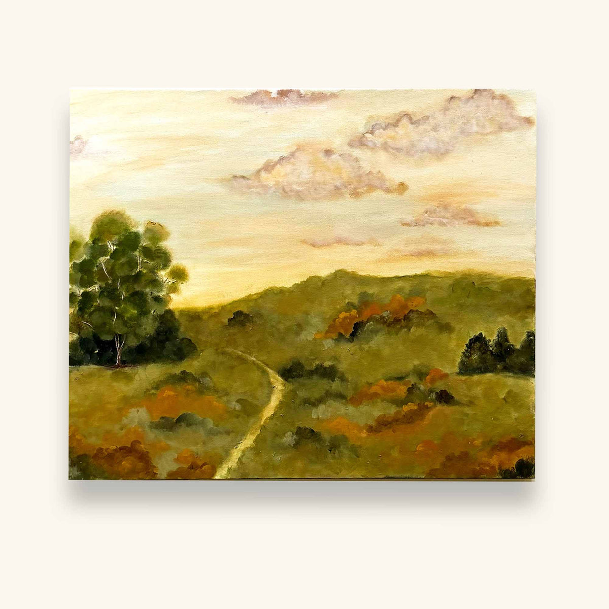 A original landscape painting by Ramya Rajiv on canvas depicting rolling green hills, a winding path, a prominent green tree on the left, and soft clouds in a pale yellow sky