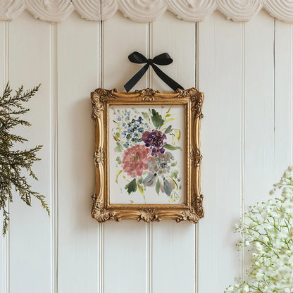 Mixed floral print in an ornate gold frame with a black ribbon on a white paneled wall.