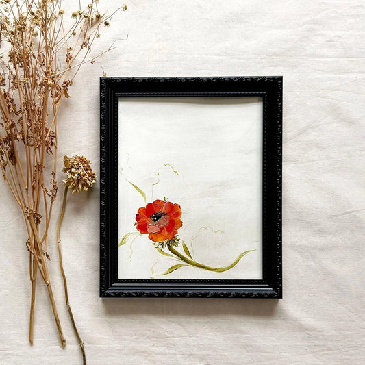 A framed floral original featuring a red anemone with green stems on an off-white background, housed in a black ornate frame 