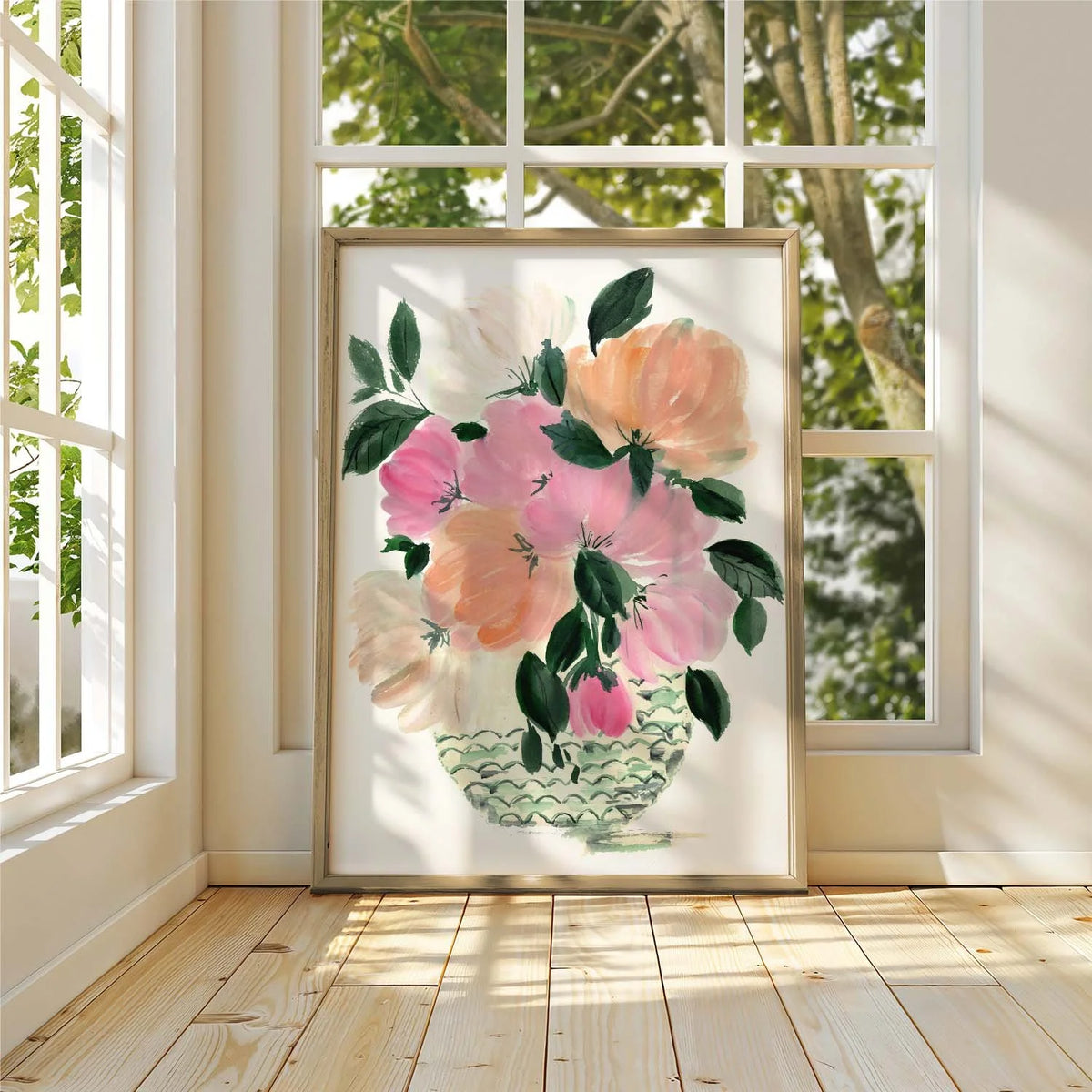 Framed pink and peach peony bouquet print leaning against a sunlit window on a wooden floor.
