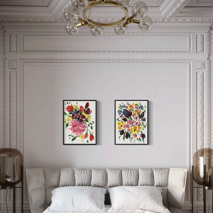 Two colorful floral prints in black frames above a tufted bed in a room with ornate white molding.