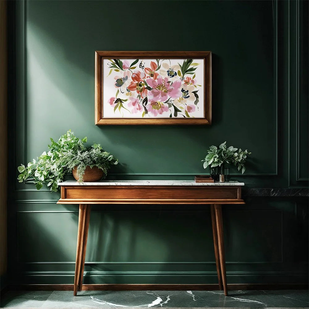 A framed floral art print hangs on a dark green paneled wall above a wooden console table with potted plants in a styled interior setting.
