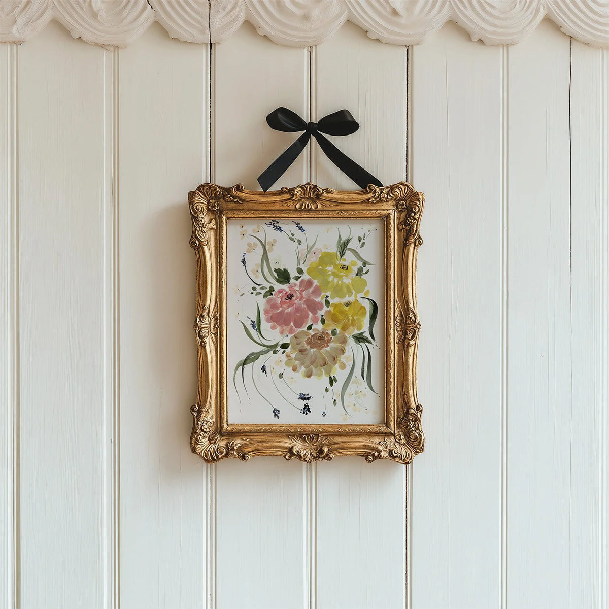 Pink and yellow ranunculus print in an ornate gold frame suspended by a black ribbon.