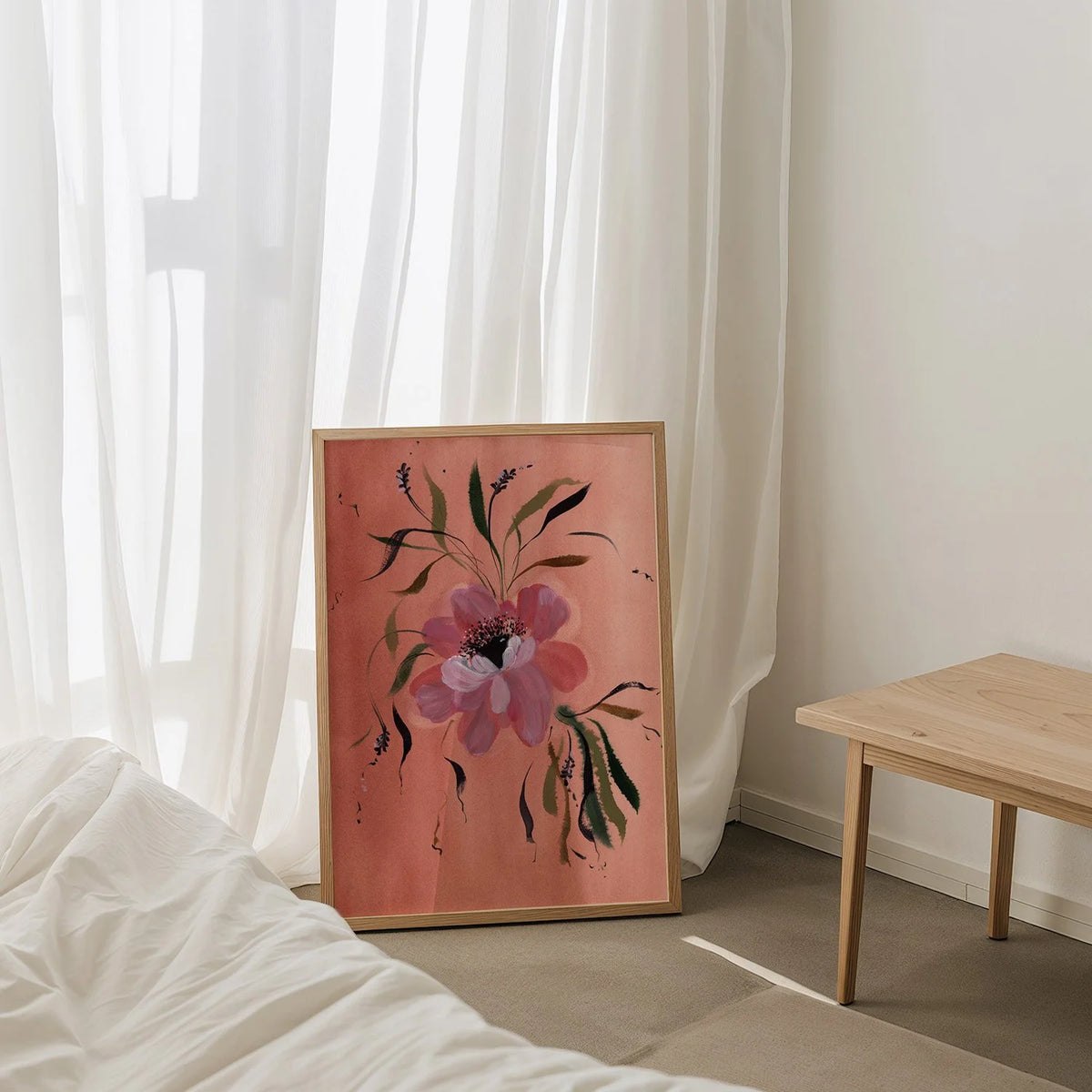 Pink anemone print on coral leaning beside sheer curtains and a wooden table.