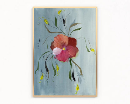 A framed floral art print featuring a large pink and red flower with green and yellow botanical details on a textured light blue background, enclosed in a thin gold frame.