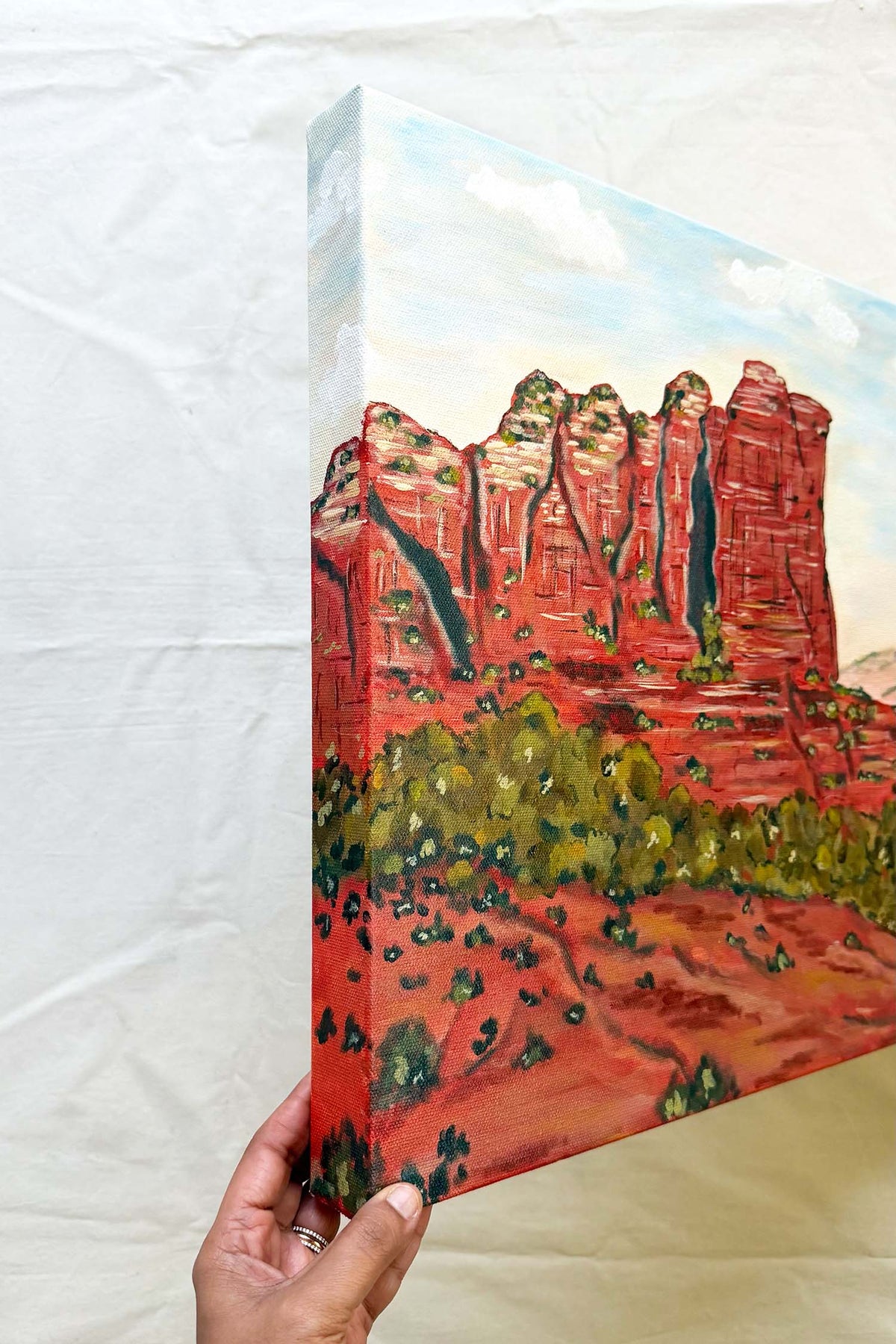 Original  painting depicting red rock desert cliffs of Sedona named Coffee Pot Rock green shrubs under a pale blue sky, by Ramya Rajiv