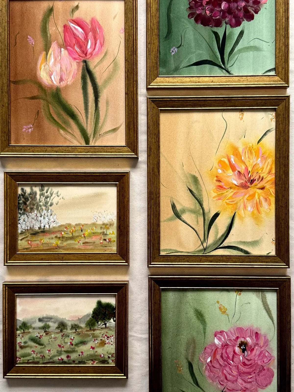 Six framed floral and landscape paintings arranged in two columns on a light wall. The frames are gold and dark brown wood, containing colorful hand-painted scenes with tulips, peonies, and fields.