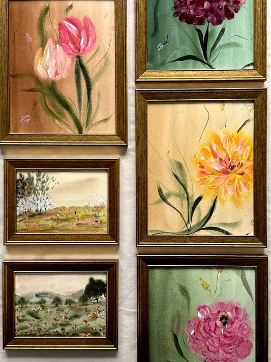 Six framed floral and landscape paintings arranged in two columns on a light wall. The frames are gold and dark brown wood, containing colorful hand-painted scenes with tulips, peonies, and fields.