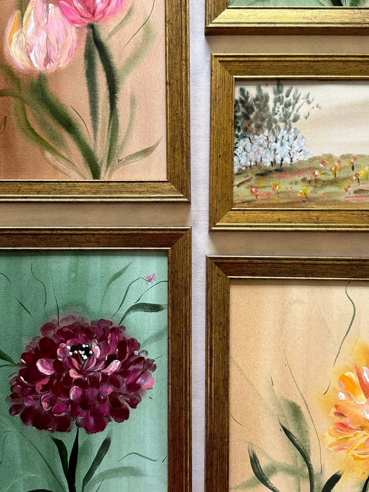 Four framed floral and landscape paintings arranged in a 2x2 grid on a light wall. The frames are gold-toned, and the artwork features pink tulips, a green floral scene, a dark purple flower, and a yellow-orange blossom.