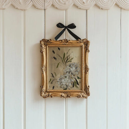 White dahlia print in an ornate gold frame suspended by a black bow on white panels.