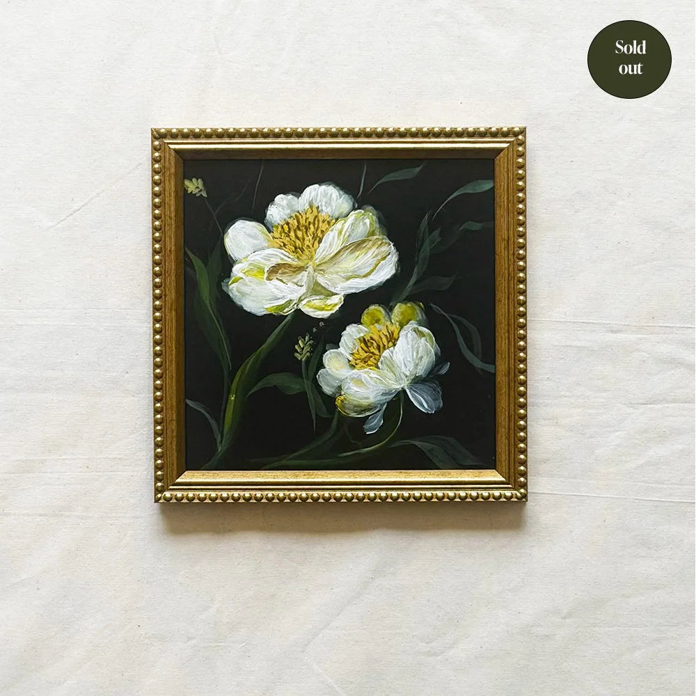 A framed oil painting of two white peony flowers with yellow centers on a dark background, housed in an ornate gold frame, displayed on a textured off-white fabric background with a 'Sold out' badge in the top right corner.