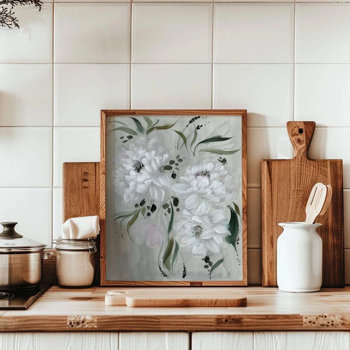 White peony print in a wood frame on a kitchen counter with cutting boards and ceramic containers.