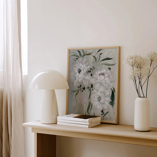 White peony print on gray resting on a wooden console beside a white lamp and vase.