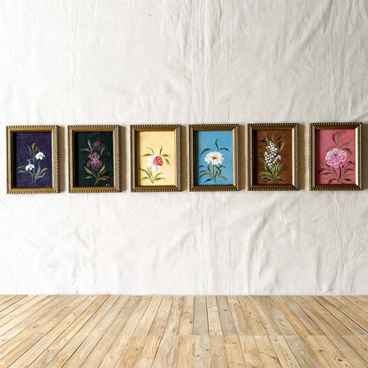 Six framed botanical original paintings in gold frames. Each painting features a flower of the month. Artwork by Ramya Rajiv