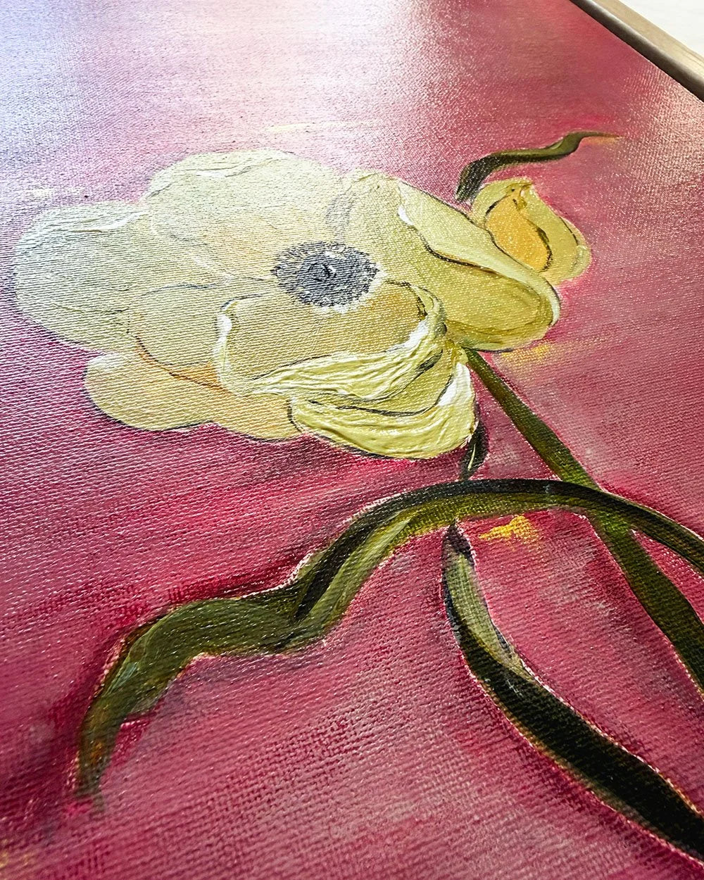 A close-up of a textured oil painting depicting a pale yellow anemone flower with a dark gray center, green stem, and a small yellow bud against a deep pinkish-red background.