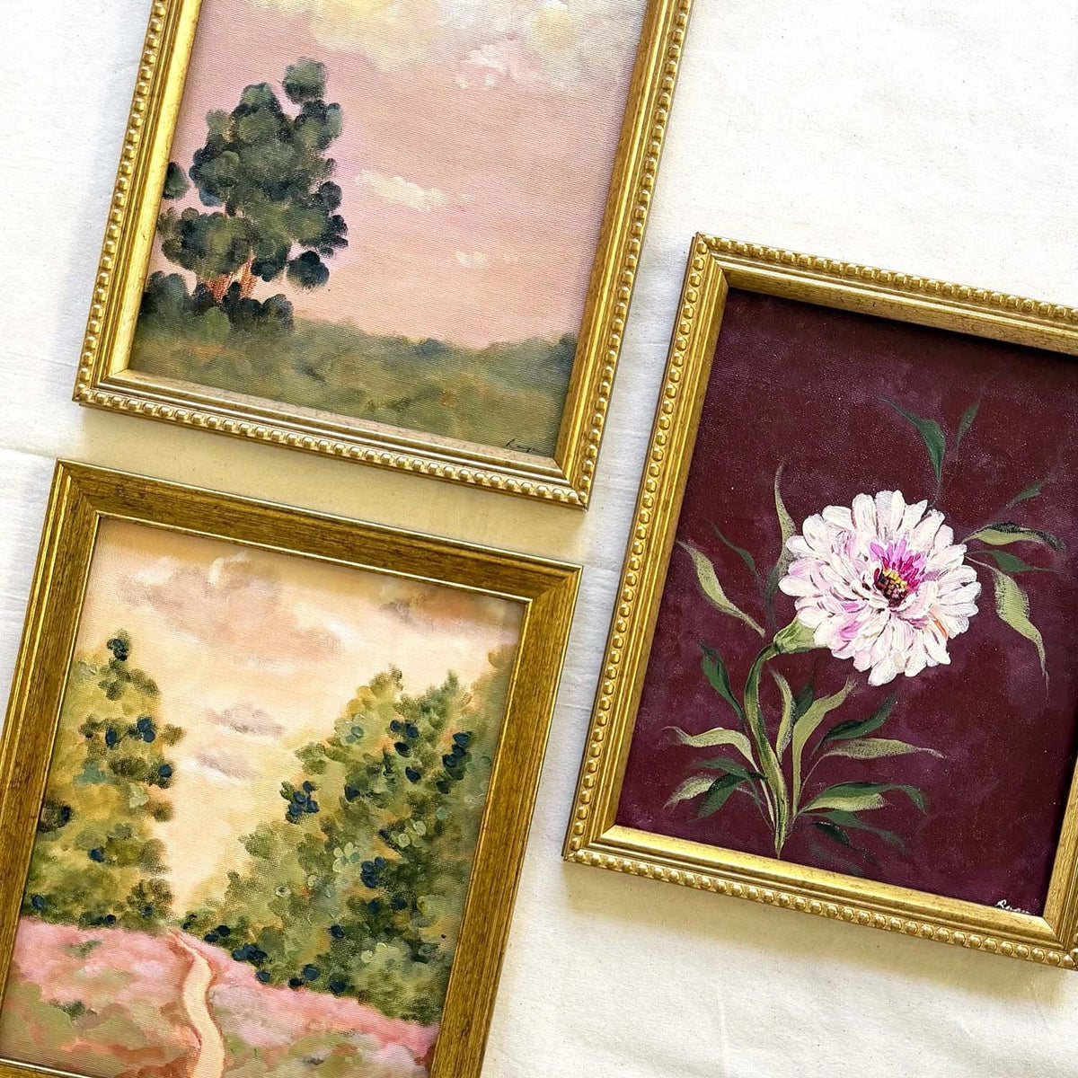 Three framed vintage watercolor paintings. One painting depicts a tree in a landscape, one shows a winding path through trees, and one features a white peony flower on a deep burgundy background with gold frames. Perfect for a gallery wall