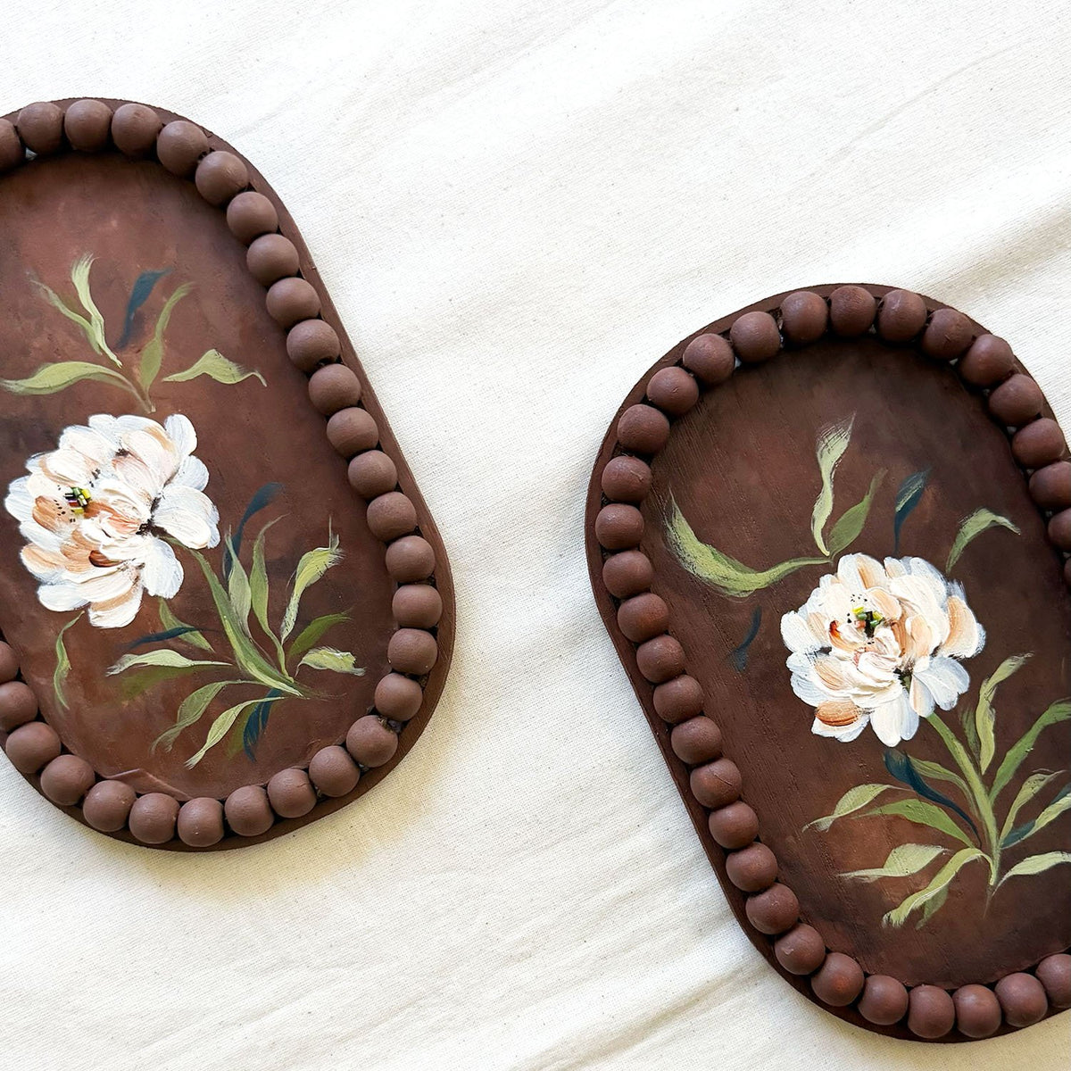 Two oval brown trays with beaded edges and hand-painted white flowers with green leaves