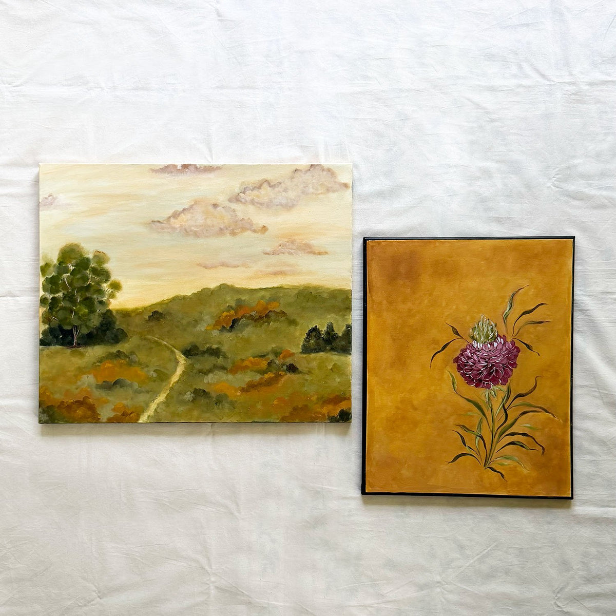 Landscape and floral original side-by-side The left painting depicts a landscape with rolling green hills, a winding path, trees, and a cloudy sky by Ramya Rajiv